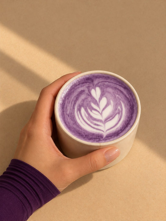 Un ube latte chaud Laya avec un latte art, tenu à deux mains