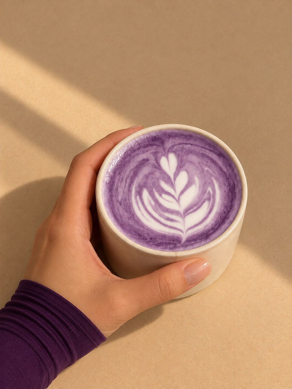 A hot Laya ube latte with latte art, held in both hands