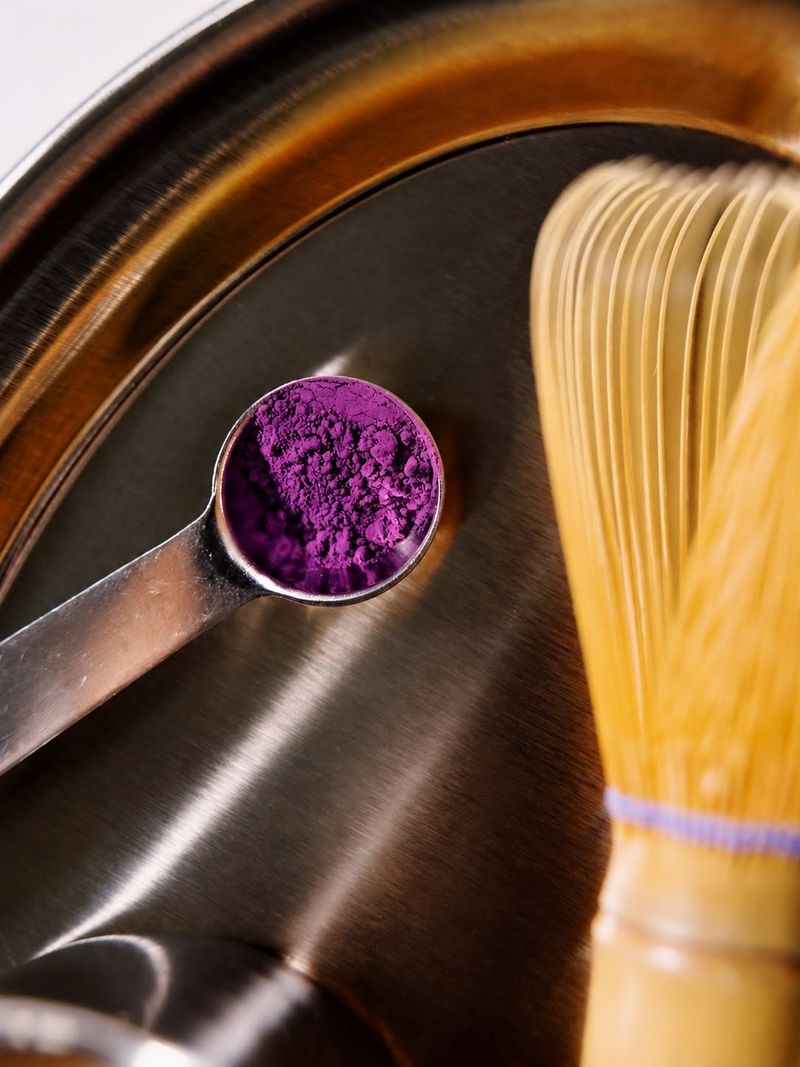 Measuring spoon filled with purple ube powder next to a bamboo whisk